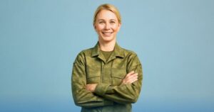 Donna in uniforme militare sorride con le braccia incrociate su sfondo azzurro, lieta per le novità che riguardano l'arrivo di aumenti e arretrati per polizia e forze armate previsti per giugno 2025