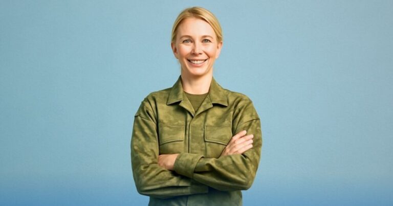 Donna in uniforme militare sorride con le braccia incrociate su sfondo azzurro, lieta per le novità che riguardano l'arrivo di aumenti e arretrati per polizia e forze armate previsti per giugno 2025